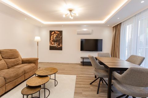 A modern living space with a comfortable couch, a table, and a television. Large windows provide plenty of daylight and a cozy atmosphere.