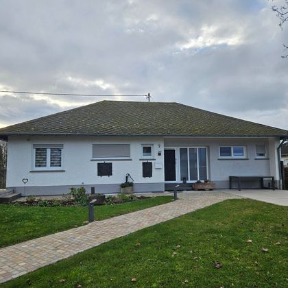 Ein modernes Einfamilienhaus mit einer einladenden Fassade und einem gepflegten Garten. Der Weg zum Eingang ist mit Steinen gepflastert und von Rasenflächen umgeben.