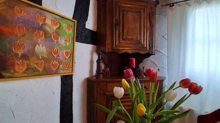 A cozy room with a wooden box and a colorful painting of tulips. On the table is a vase with fresh tulips in various colors.