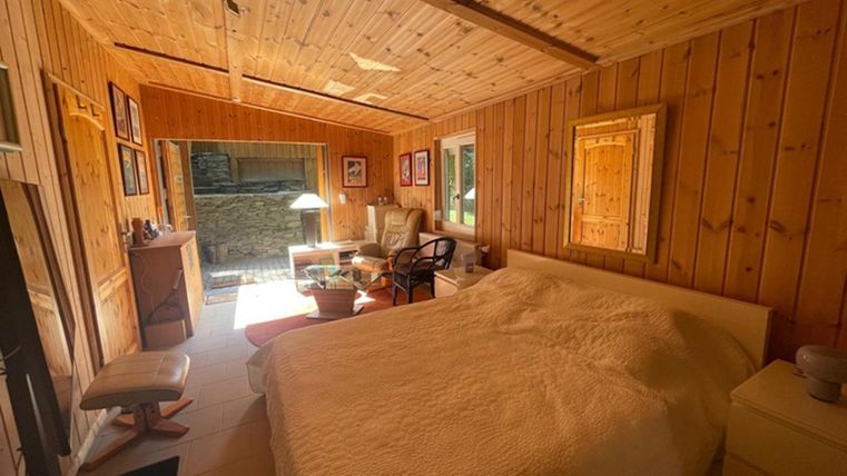 A cozy bedroom with wood paneling and a large bed. There is a window that looks out onto a green oasis, as well as a few pieces of furniture that make the room inviting.