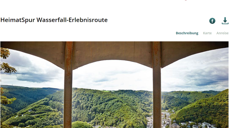 Eine beeindruckende Aussicht auf eine grüne Hügellandschaft mit einem Fluss im Tal. Im Vordergrund sind die Stützpfeiler einer Brücke sichtbar.