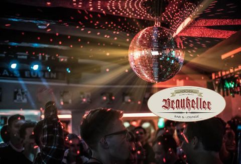 A lively bar with dancing people and a sparkling disco ball. Colorful lights create a festive atmosphere.