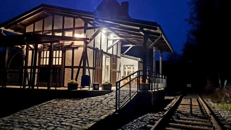 Une vieille maison de gare éclairée la nuit. Les chemins de pierre et les voies de chemin de fer passent juste à côté.
