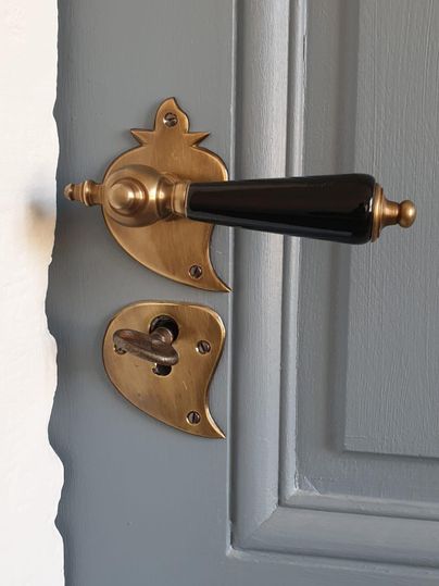 An elegant door with an antique brass door handle and a black edge. The fitting features a unique design that complements the gray wall color.