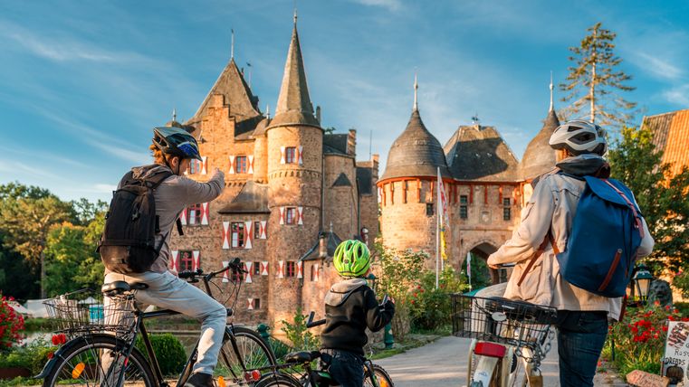 Drie fietsers voor het kasteel van Satzvey bij zonnig weer.