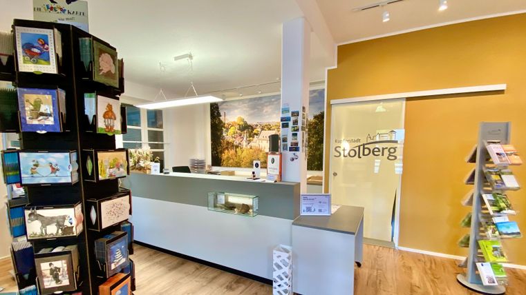 Een moderne receptie met een balie en een informatiepunt. Aan de linkerkant staan ansichtkaarten en brochures.