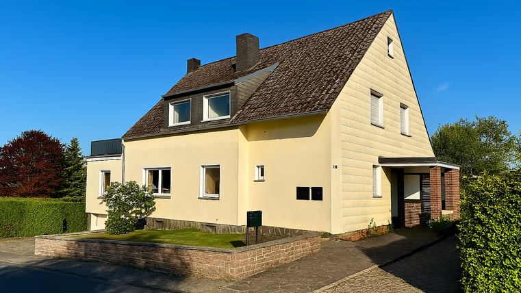 Ein schönes Einfamilienhaus in Gelb mit einem schrägen Dach und grüner Bepflanzung. Der Himmel ist klar und blau.