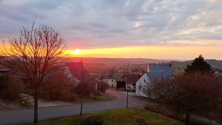 Un coucher de soleil pittoresque sur un paysage tranquille.
Des maisons et des arbres encadrent la scène, tandis que le ciel brille de couleurs chaudes.