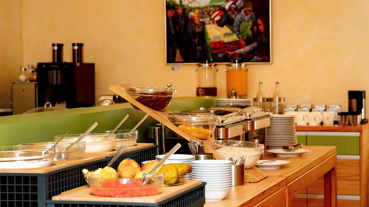 A rich breakfast buffet with a selection of fresh fruit, yogurt, and snacks. In the background, there is a colorful painting.