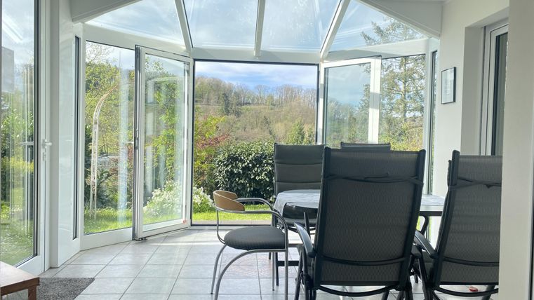 A cozy winter garden with open windows. In the background, green plants and a tranquil landscape can be seen.