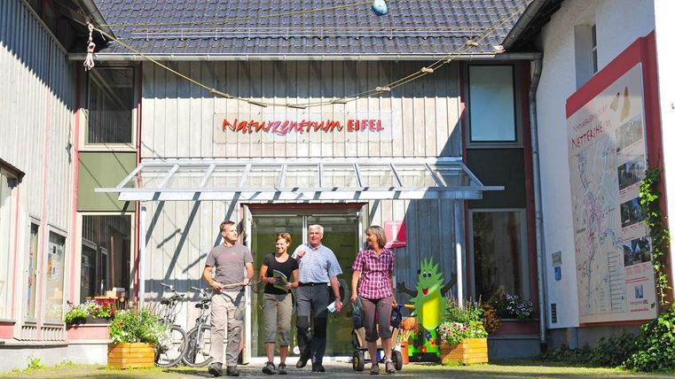 Een natuurminnend centrum met een modern gebouw. Vier personen staan voor de ingang en poseren vriendelijk.