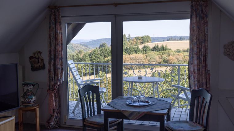 A cozy living space with a table and chairs that offers a view of the hilly landscape. Outside, there is a small balcony with a table and chairs.