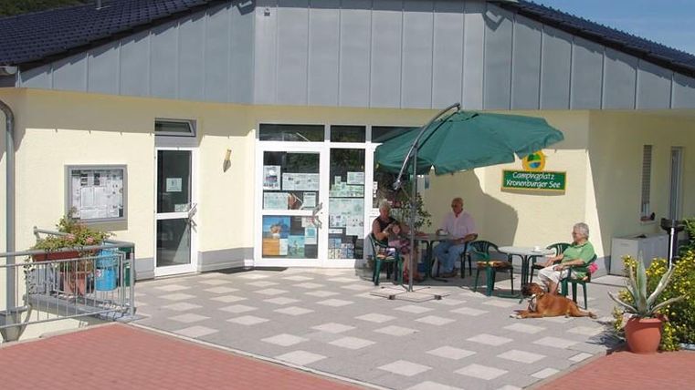 View of the entrance area of the bistro.
A yellow-painted building with two entrance doors.
In front of the house is a paved terrace with several tables and chairs.