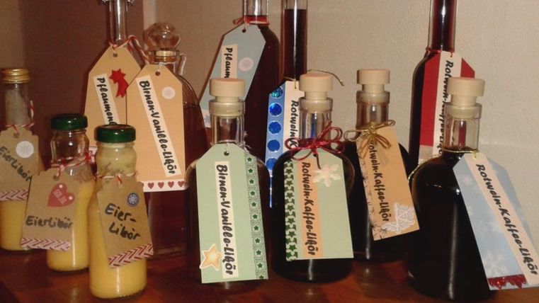 Une série de bouteilles avec différents liqueurs est disposée sur une table. Chaque bouteille a une étiquette avec une description du contenu.