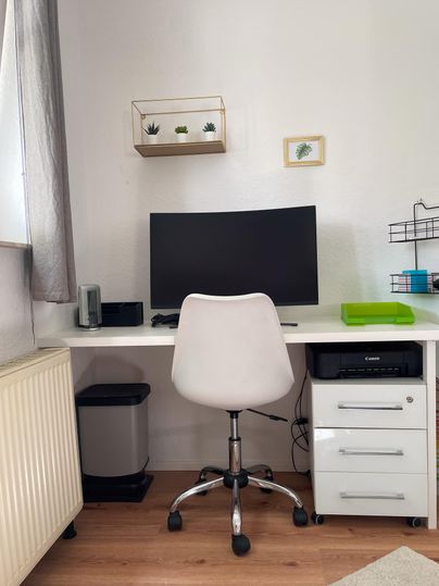 A modern desk with a computer monitor and a white office chair. A printer is also on site.