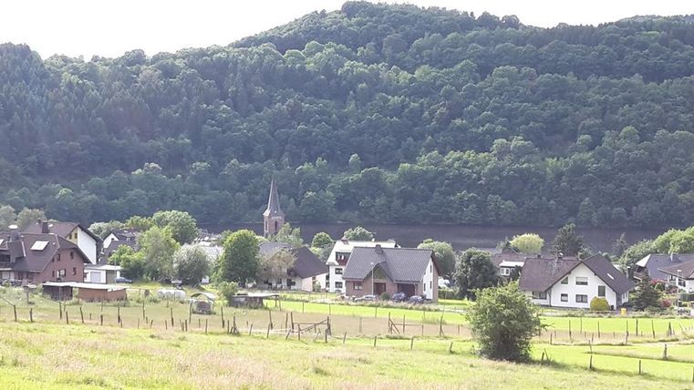 Een rustig landschap met een klein dorp en een kerk in het midden. Op de achtergrond zijn groene heu vel en bomen te zien.