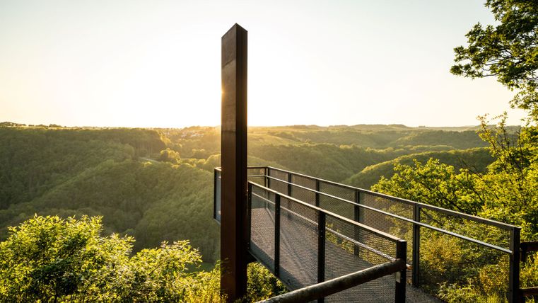 Skywalk am Eifelblick Achterhöhe mit Blick auf bewaldete Hügel bei Sonnenuntergang.