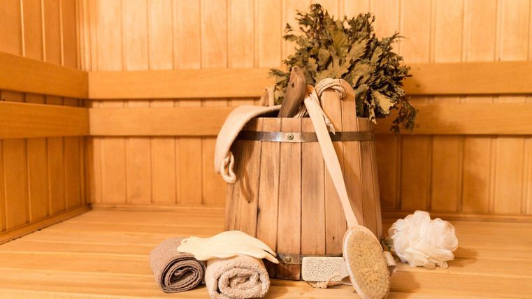 A wooden bucket with sauna accessories, towels, and a ladle in a wooden sauna.