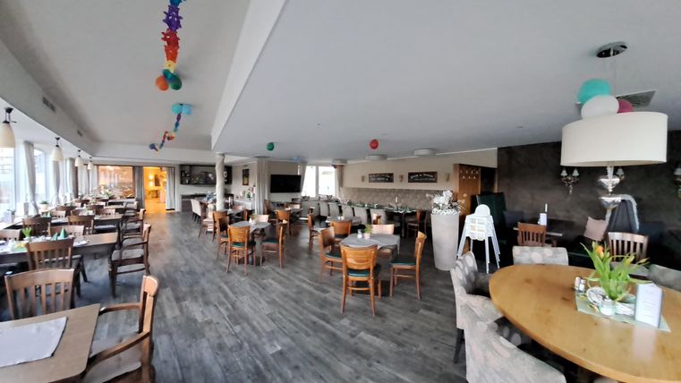 A modern restaurant with wooden furniture and large windows. The room is bright and friendly, decorated with colorful elements.