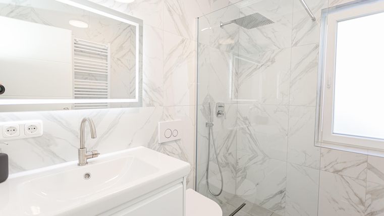 A modern bathroom with a bright marble look and a walk-in shower. The sink area is clean and well-lit.