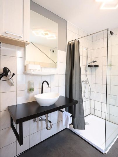 A modern bathroom with a glass shower area and an elegant sink arrangement. The walls are tiled with white tiles and a mirror reflects the space.