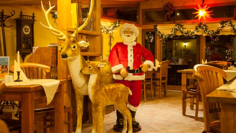 Een feestelijk versierd restaurant met een kerstman en twee houten rendieren. De gezellige sfeer wordt benadrukt door de lichten en versieringen.
