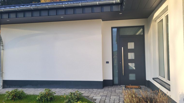 Een modern huis met een grijze deur en een strakke tuin. Het pad is geplaveid met stenen en de gevel is eenvoudig en elegant.