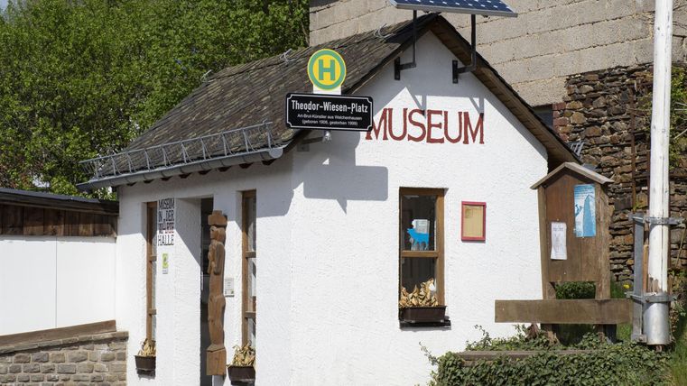 Ein kleines Museum mit weißer Fassade und einem Sonnensystem auf dem Dach. Es liegt an einer Straße mit einem Haltestellenschild in der Nähe.