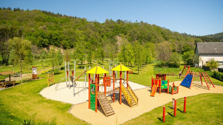 A beautiful playground with colorful play equipment and green trees in the background. The sunny sky creates an inviting atmosphere.