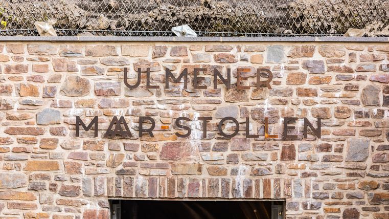 Auf einer Steinwand die Aufschrift „Ulmener Maar- Stollen“ über dem Eingang 