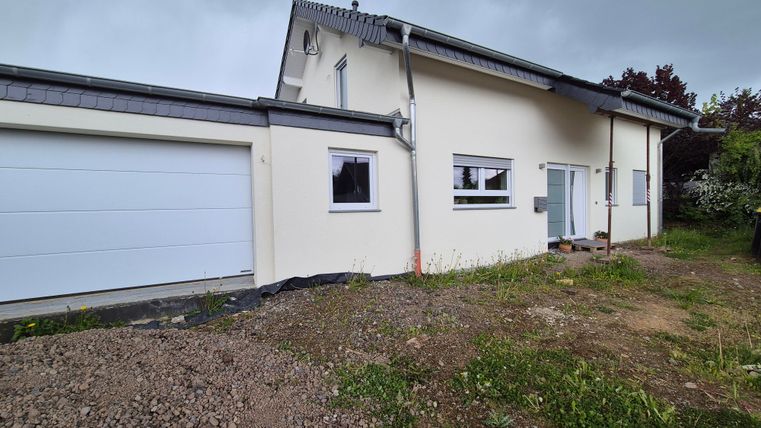 Ein modernes Haus mit einer Garage und großen Fenstern. Der Garten ist noch unordentlich mit frischem Gras und Erde.