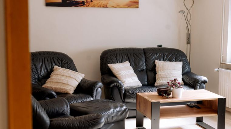 A cozy living room with black leather sofas and a wooden table. A modern picture hangs on the wall and there is a floor lamp.