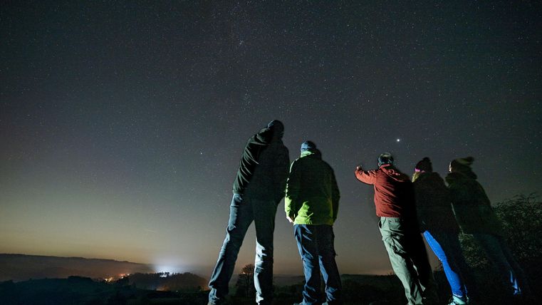 Un groupe de personnes se tient sous le ciel étoilé la nuit. Ils regardent le ciel et montrent les étoiles.
