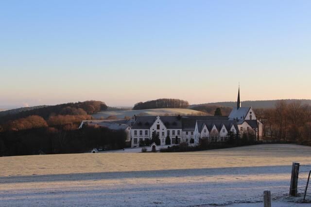 Un bâtiment historique en hiver, entouré d'herbe légèrement gelée et de douces collines. Le ciel est clair et le paysage dégage une sensation de calme.