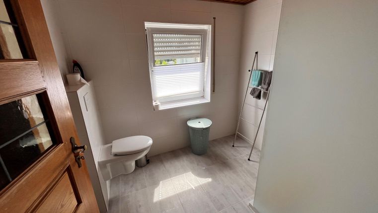 A modern bathroom with a white toilet and a green toilet. The room has bright tiles and a wooden ceiling.