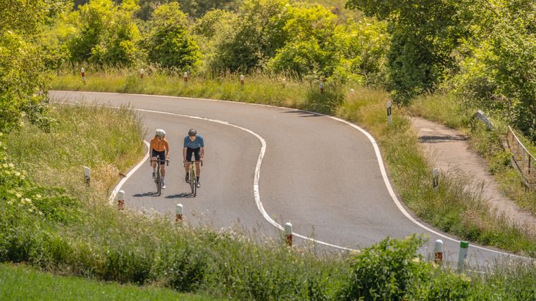 Twee fietsers op een kronkelende landweg in de Eifel.
