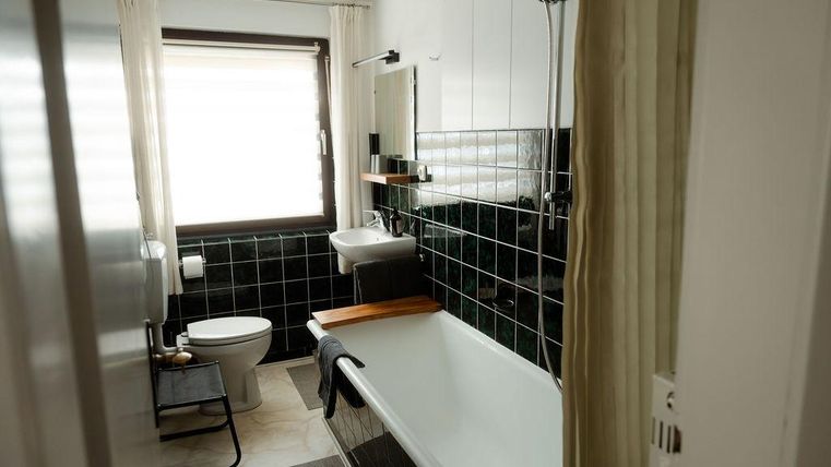 Une salle de bain moderne avec une baignoire et une douche.
Il y a un lavabo, une toilette et de grandes fenêtres avec des rideaux.