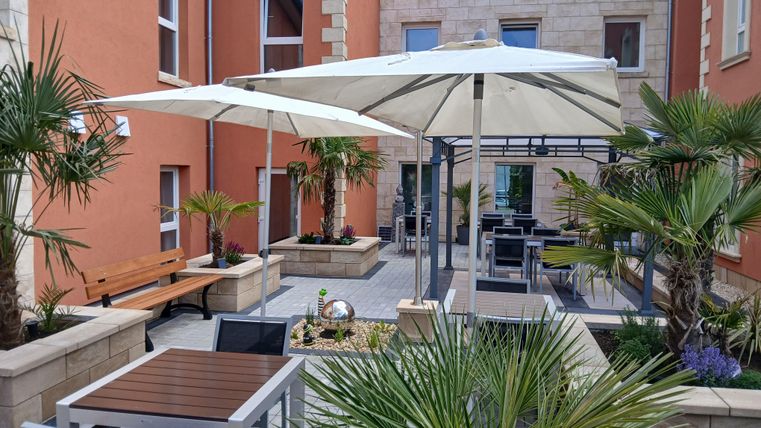 Ein gemütlicher Innenhof mit Palmen und Sonnenschirmen. Es gibt Tische und Stühle, die zum Entspannen einladen.