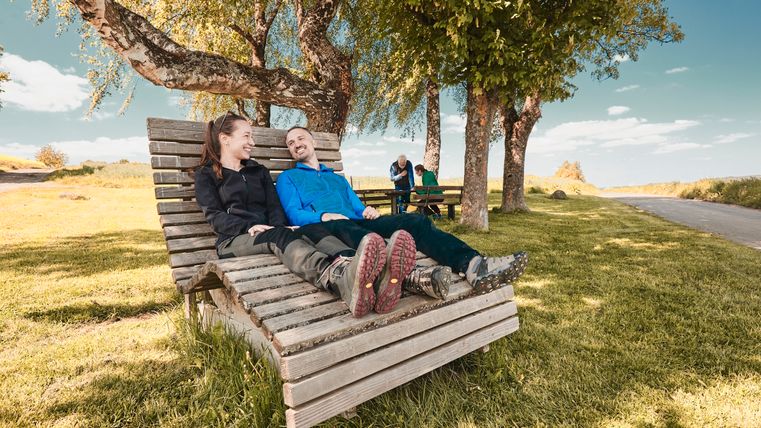 Deux personnes font une pause sur une chaise longue en bois.