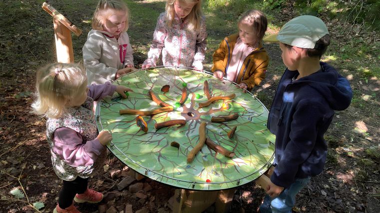 Kinder spielen an einem runden Tisch im Wald.