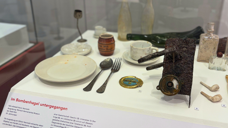 In einer Vitrine liegen mehrere Alltagsgegenstände mit starken Beschädigungen.