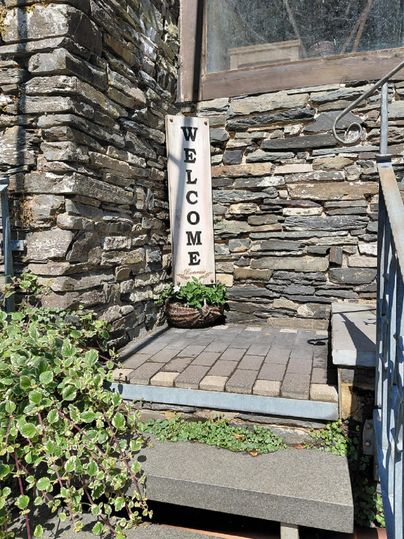 An inviting stone entrance with a welcome sign. Planters and green plants create a friendly atmosphere.