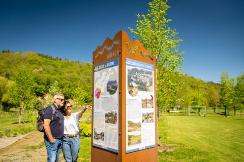 A couple is looking at an information booth in a green park landscape. The sun is shining and the surroundings are calm and inviting.