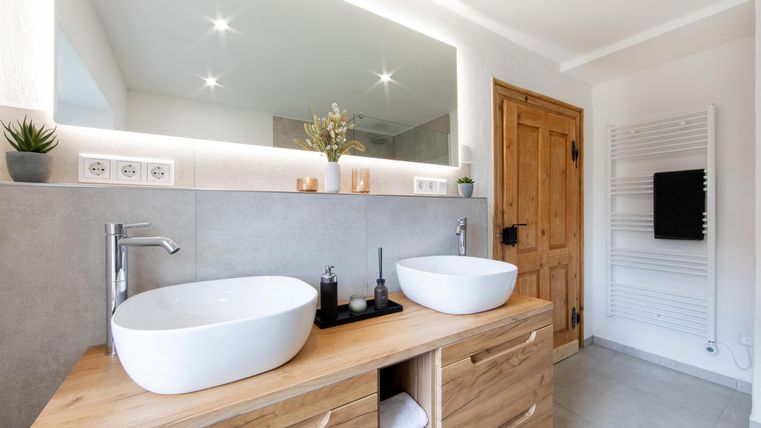 Ein modernes Badezimmer mit zwei Waschbecken auf einem Holzschrank. Große Spiegel und sanfte Beleuchtung schaffen eine einladende Atmosphäre.