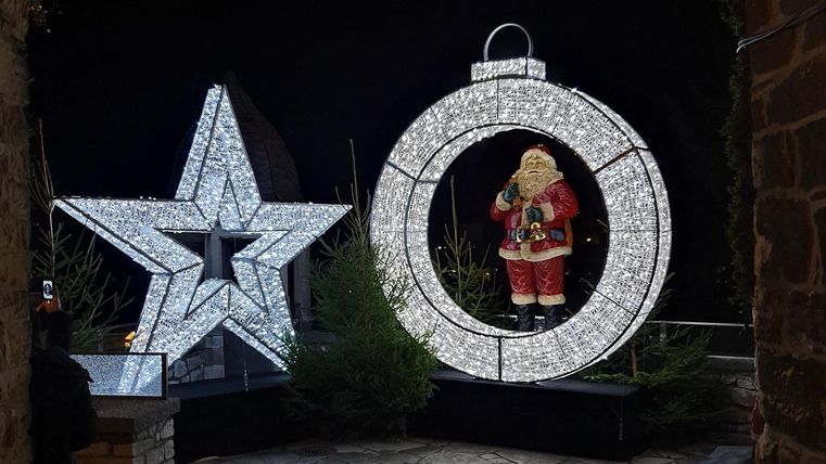 Ein festlich dekorierter Bereich mit einem beleuchteten Weihnachtsmann in einem großen Ring und einem strahlenden Stern. Die Szene strahlt festliche Stimmung und weihnachtliche Freude aus.