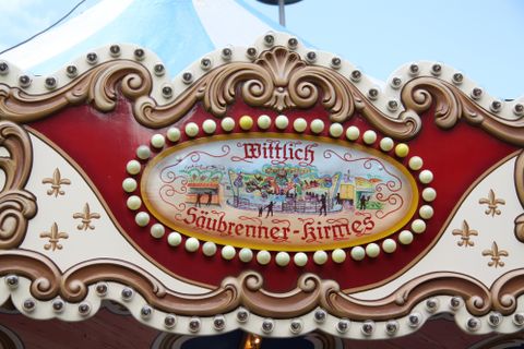 A decorative sign with the text "Wittlich Sauwerner Kirmes". It features a colorful illustration of festivities.