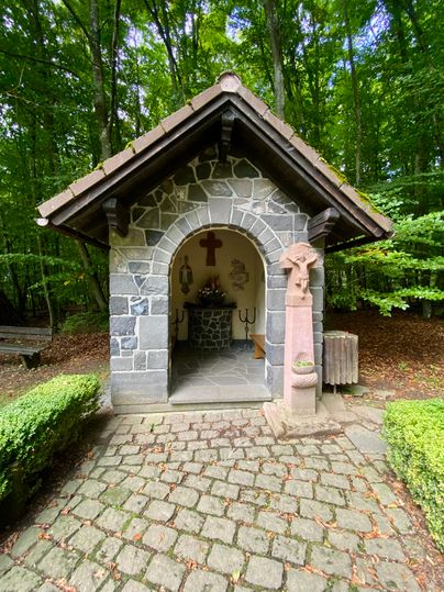 The small Arnulphus Chapel with altar and painted walls inside, in front of a deciduous forest.
