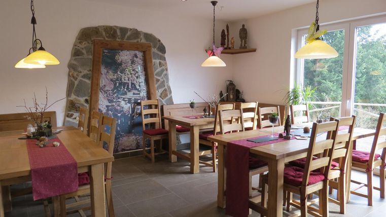 A cozy restaurant with wooden tables and chairs. The walls are light and there are large windows that let in a lot of light.