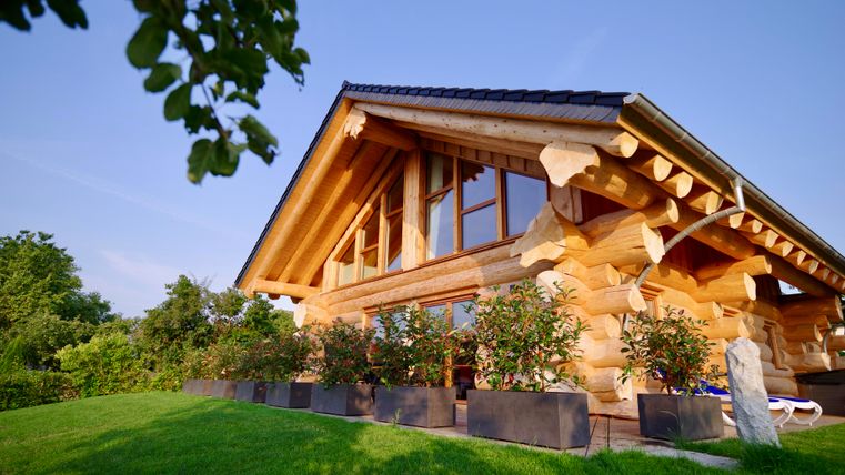 Une maison en bois moderne avec de grandes fenêtres et un toit à deux versants. Le jardin est vert et a des pots de fleurs décoratifs.