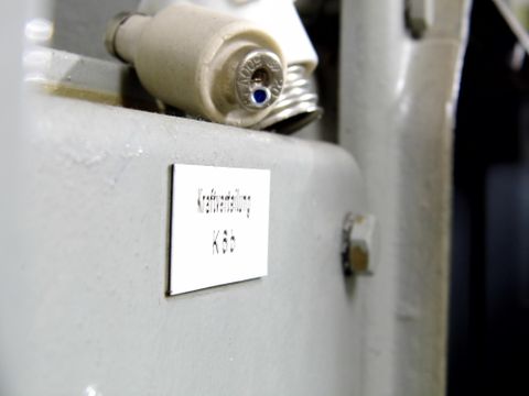 Ein naher Blick auf eine Metalloberfläche mit einem Etikett. Das Etikett zeigt eine technische Bezeichnung und ist an einer Maschine angebracht.